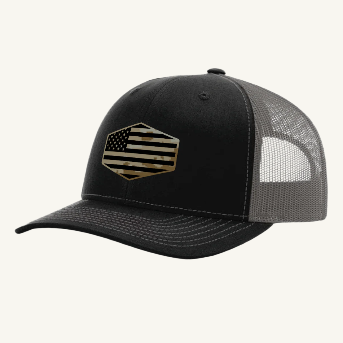 A black and charcoal trucker hat with a digicam acrylic patch featuring the US flag in a desert storm camouflage pattern on the front.