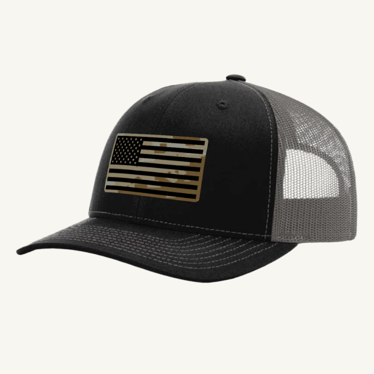 A black and charcoal trucker hat with a digicam acrylic patch featuring the US flag in a desert storm camouflage pattern on the front.