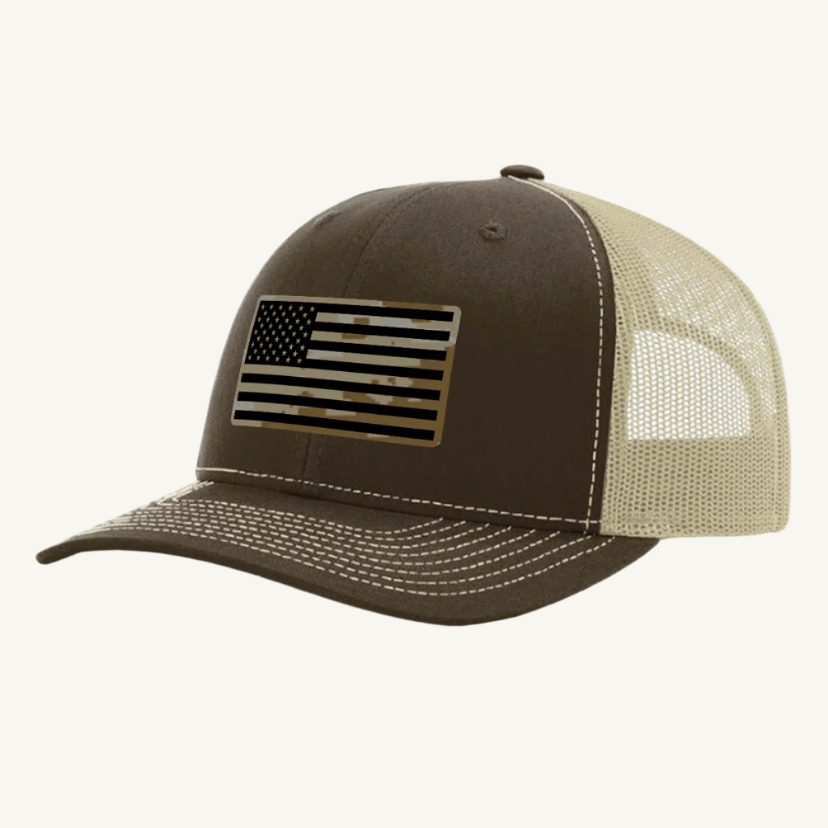 A brown and khaki trucker hat with a digicam acrylic patch featuring the US flag in a desert storm camouflage pattern on the front.