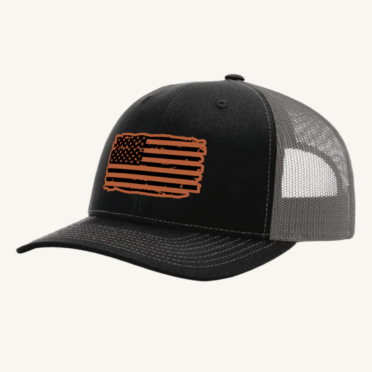 A black and charcoal trucker hat with a distressed American flag design on the front, featuring a leatherette patch.