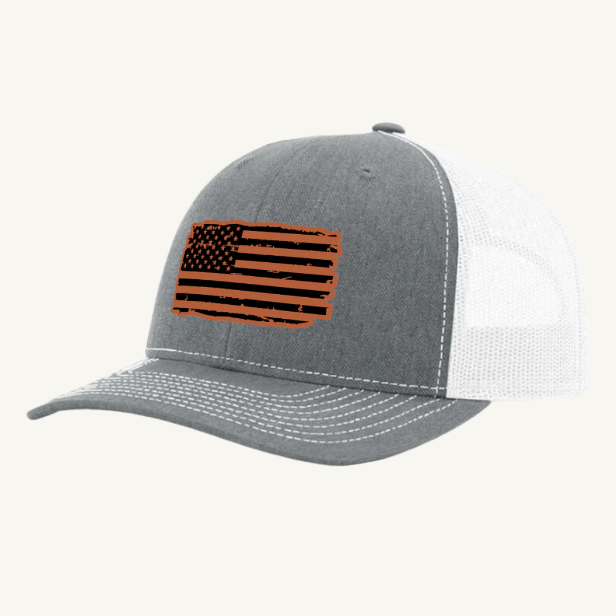 A heather gray and white trucker hat with a distressed American flag design on the front, featuring a leatherette patch.
