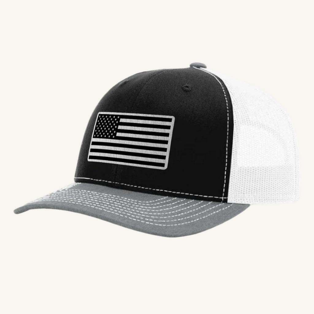 A heather gray, black, and white trucker hat with a stainless steel acrylic patch featuring an American flag design on the front.