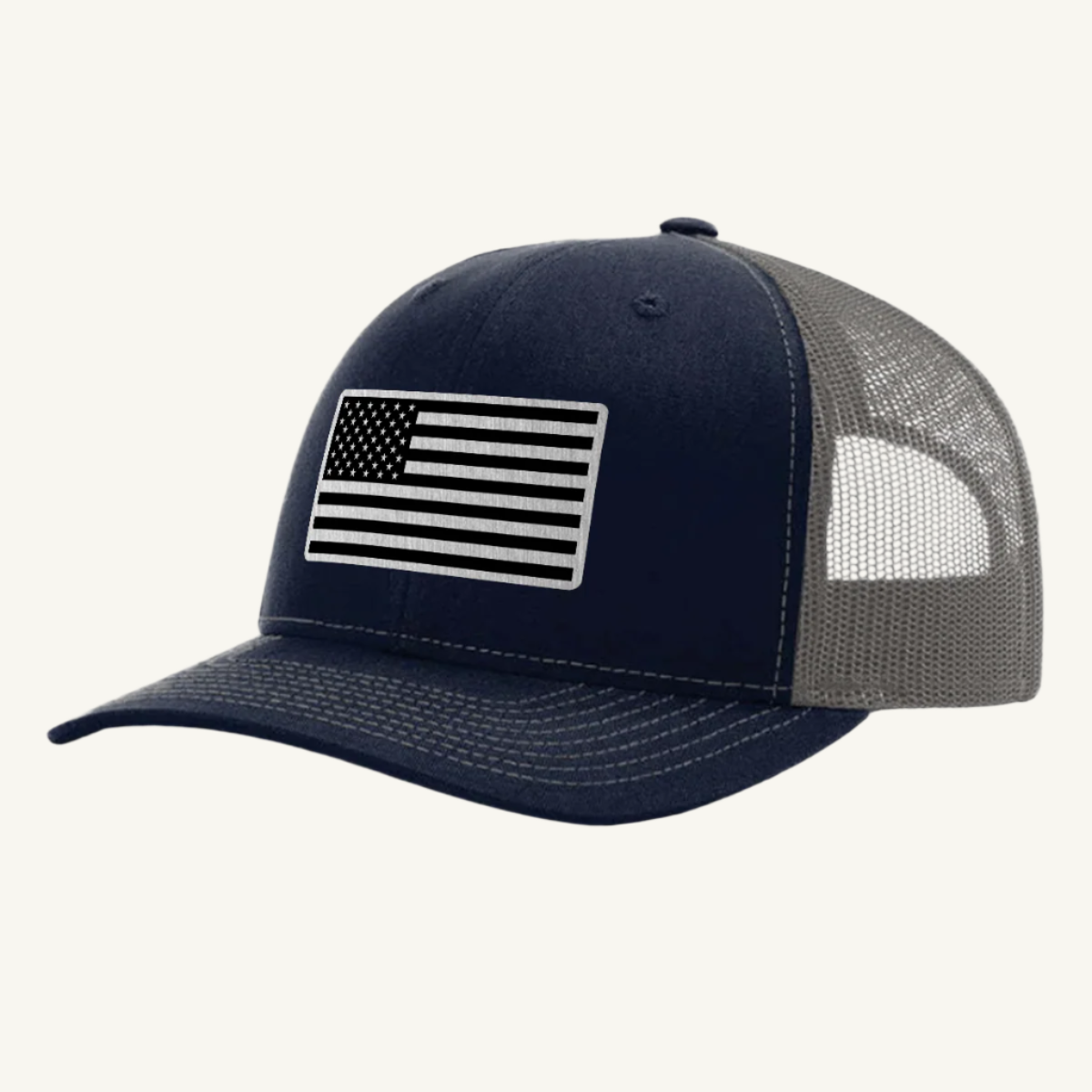 A navy blue and gray trucker hat with a stainless steel acrylic patch featuring an American flag design on the front.