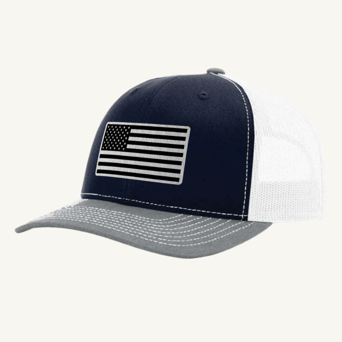 A heather gray, navy blue, and white trucker hat with a stainless steel acrylic patch featuring an American flag design on the front.