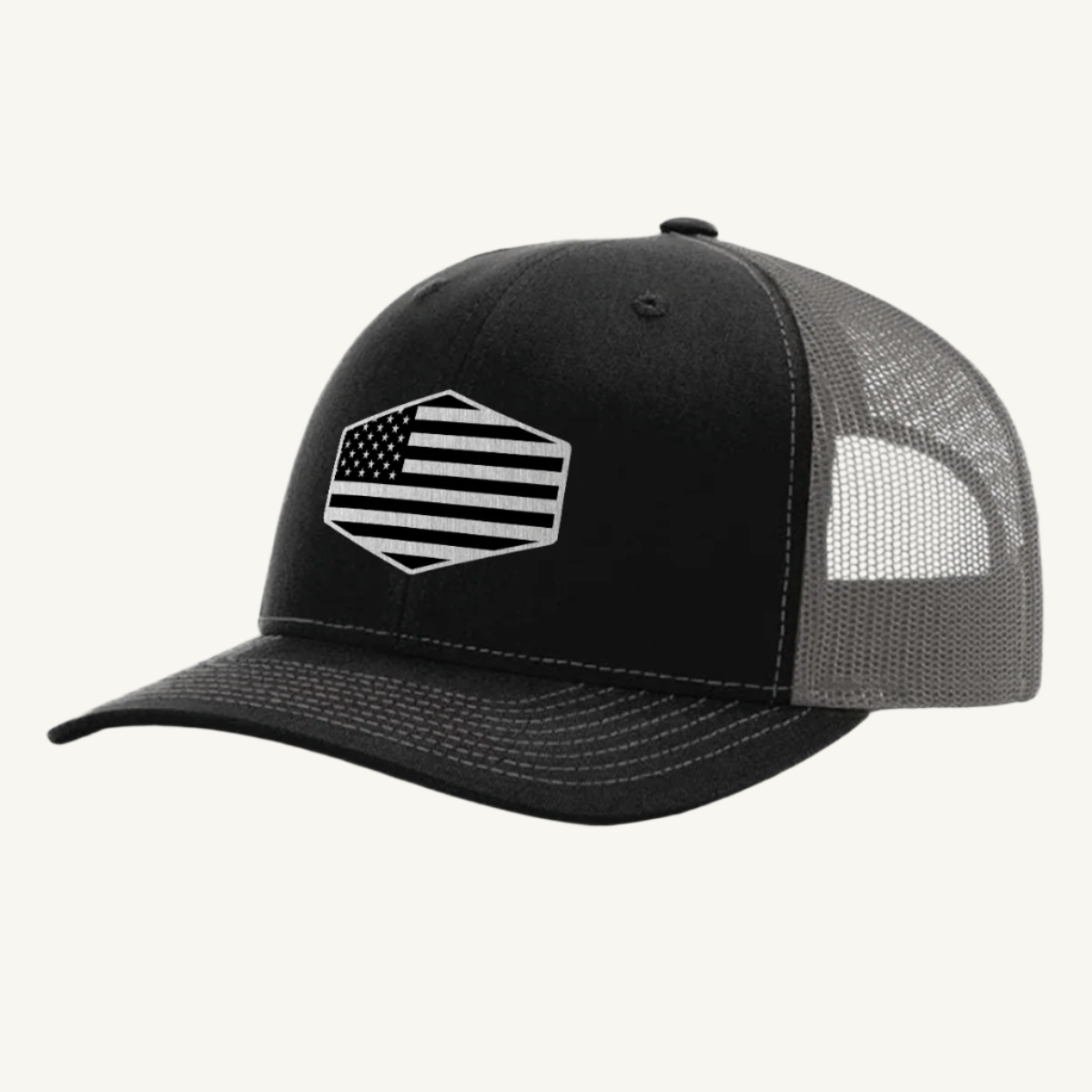 A black and charcoal trucker hat with a stainless steel acrylic patch featuring an American flag design on the front.