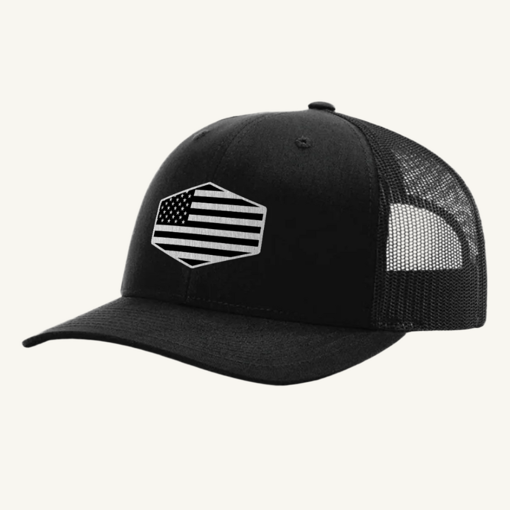 A black trucker hat with a stainless steel acrylic patch featuring an American flag design on the front.