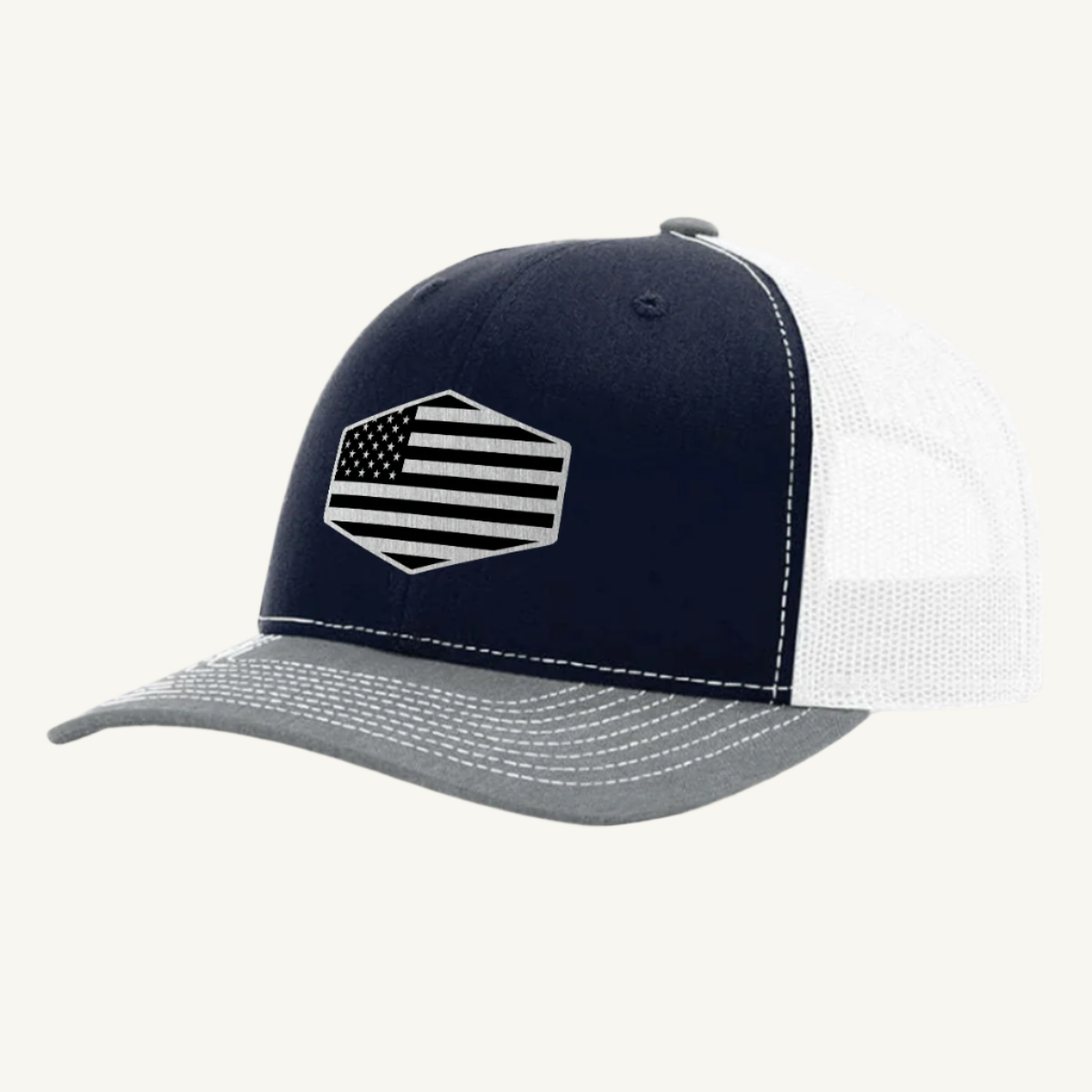 A heather gray, navy blue, and white trucker hat with a stainless steel acrylic patch featuring an American flag design on the front.