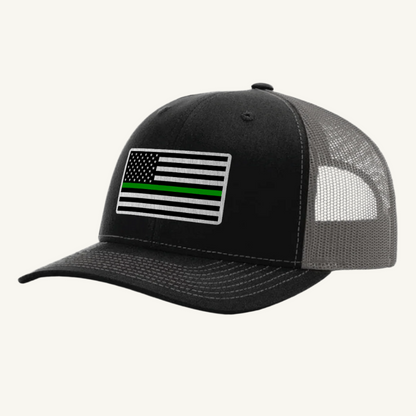 A black and gray trucker hat with an acrylic patch on the front displaying the Thin Green Line American Flag.