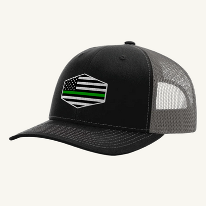 A black and gray trucker hat with an acrylic patch on the front displaying the Thin Green Line American Flag.